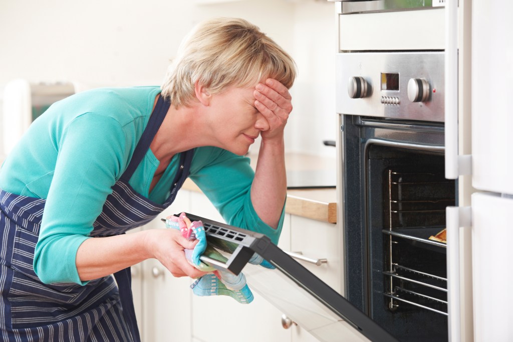 Woman covering her eyes as she watches a disastrous meal in the oven